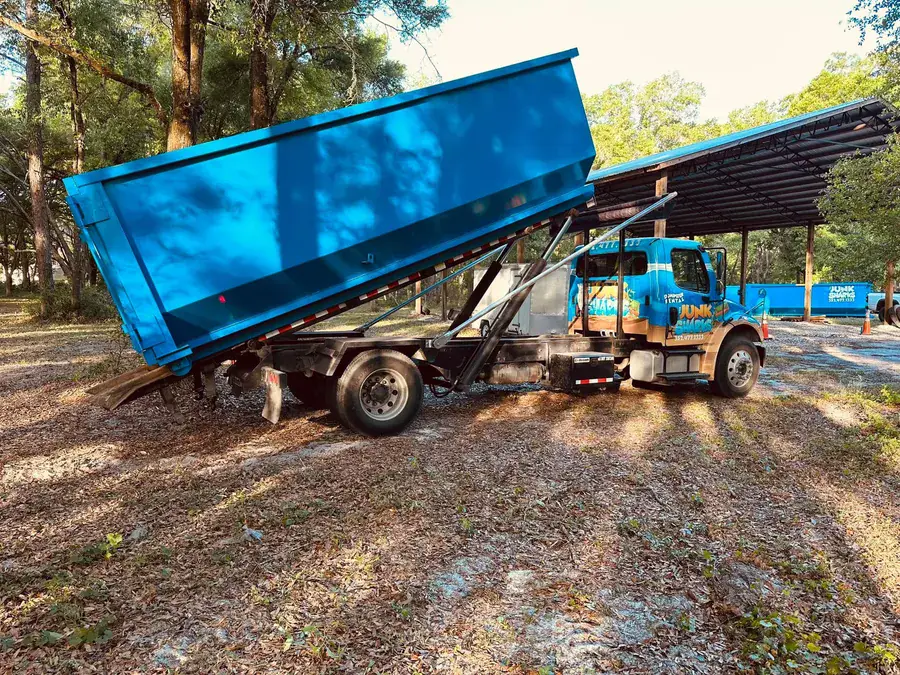 A branded Junk Sharks truck delivering a dumpster